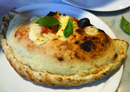 Calzone doré, garni de fromage et herbes, servi sur une assiette blanche.