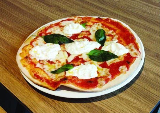 Pizza garnie de sauce tomate, mozzarella, basilic et morceaux de fromage crémeux.