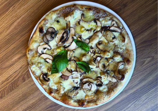 Pizza garnie de champignons, fromage, ananas et feuilles de basilic sur une croûte dorée.