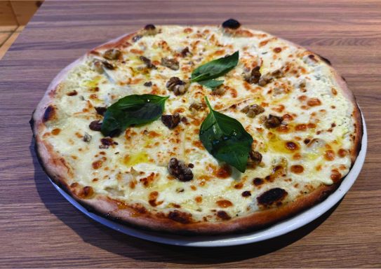 Pizza blanche avec champignons et feuilles de basilic sur une croûte dorée.