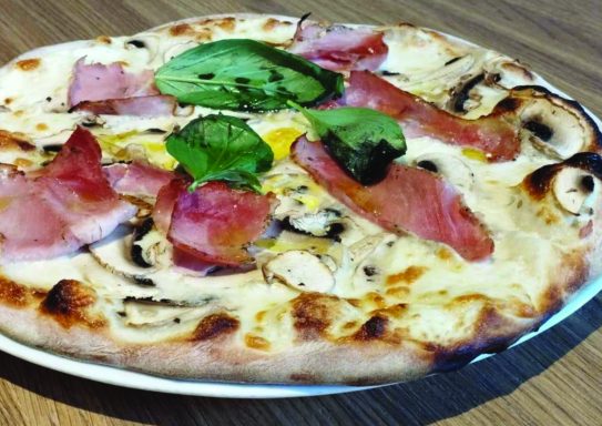 Pizza garnie de jambon, œuf, champignons et épinards, sur une pâte dorée.