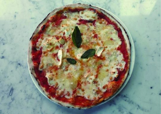 Pizza margherita garnie de feuilles de basilic sur une surface en marbre.