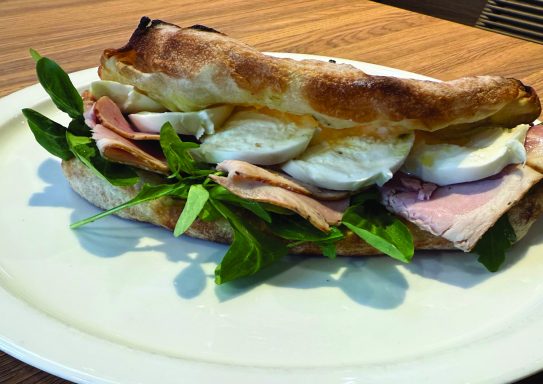 panuozzo classique Sandwich garni de jambon, mozzarella et verdure, reposant sur une assiette blanche.