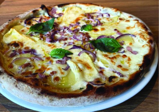 Pizza garnie de fromage, lardons, oignons rouges et feuilles de basilic.